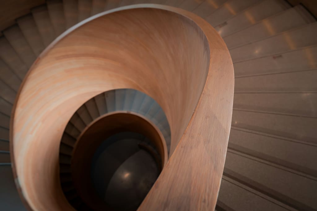 An internal stairwell with a plain handrail, clear treads and daylight from a side window.