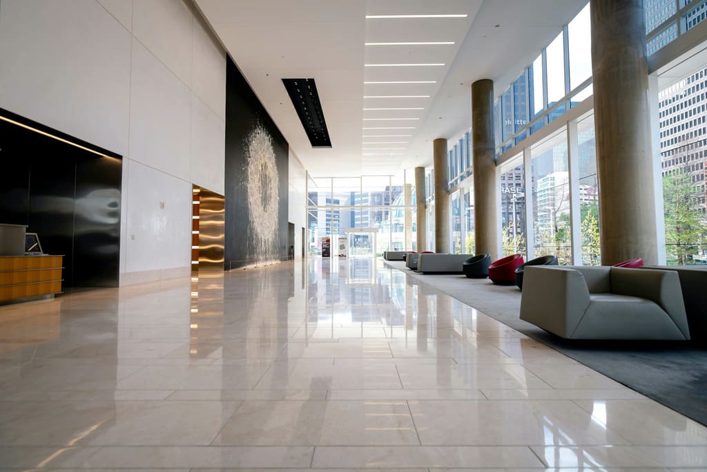 A calm building lobby with polished floors, a reception desk and clear entrance glazing.